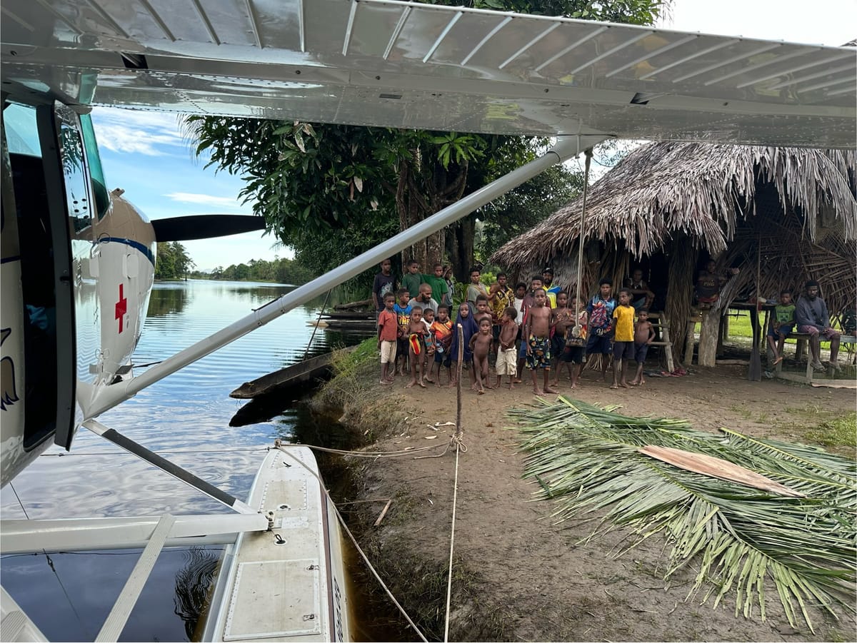 Cessna 206 amphibious floatplane parked next to a village house in Papua New Guinea.